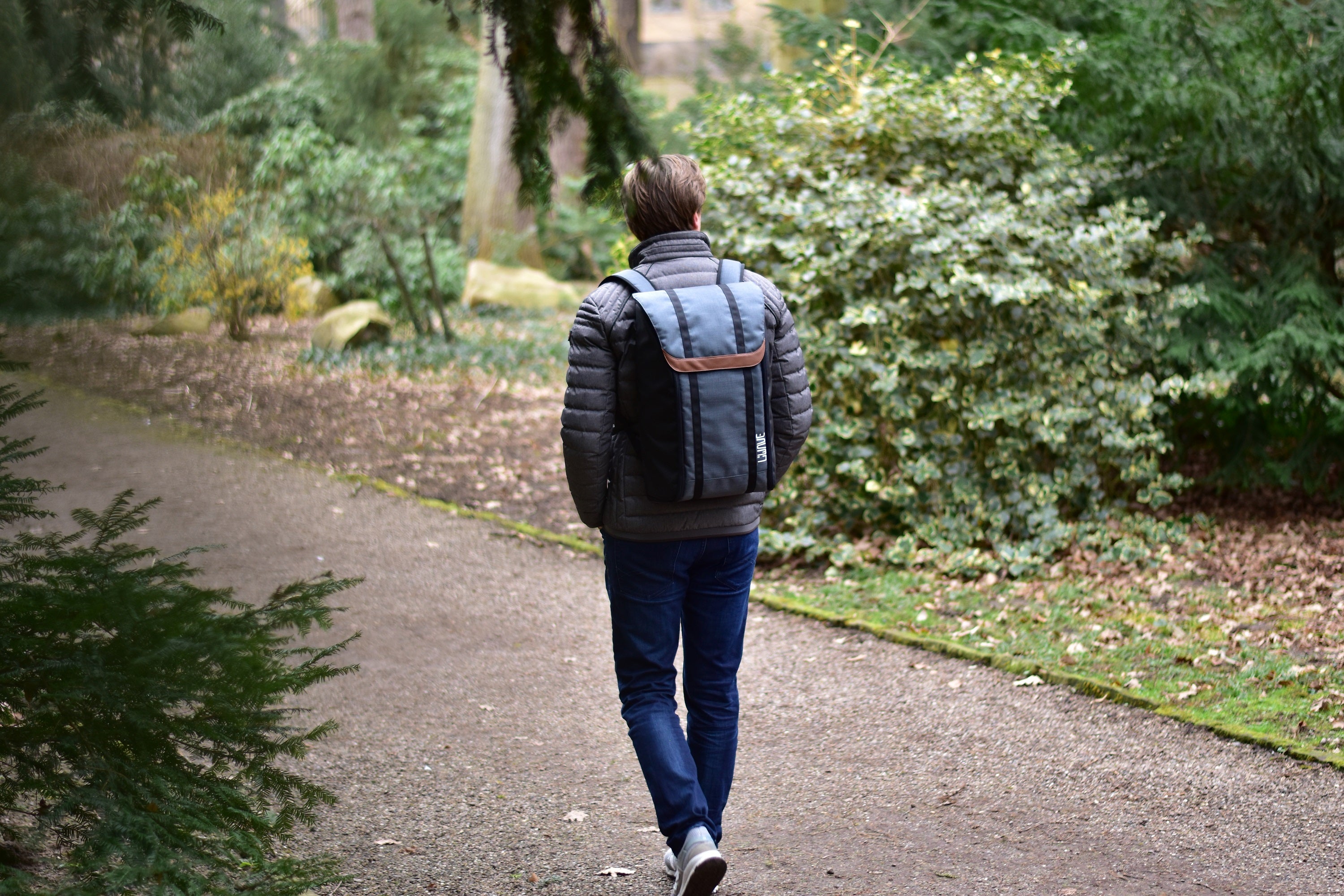 Mann mit blauem LiWAVE Rucksack auf dem Rücken in der Natur mit grünen Bäumen und Buschen geht spazieren