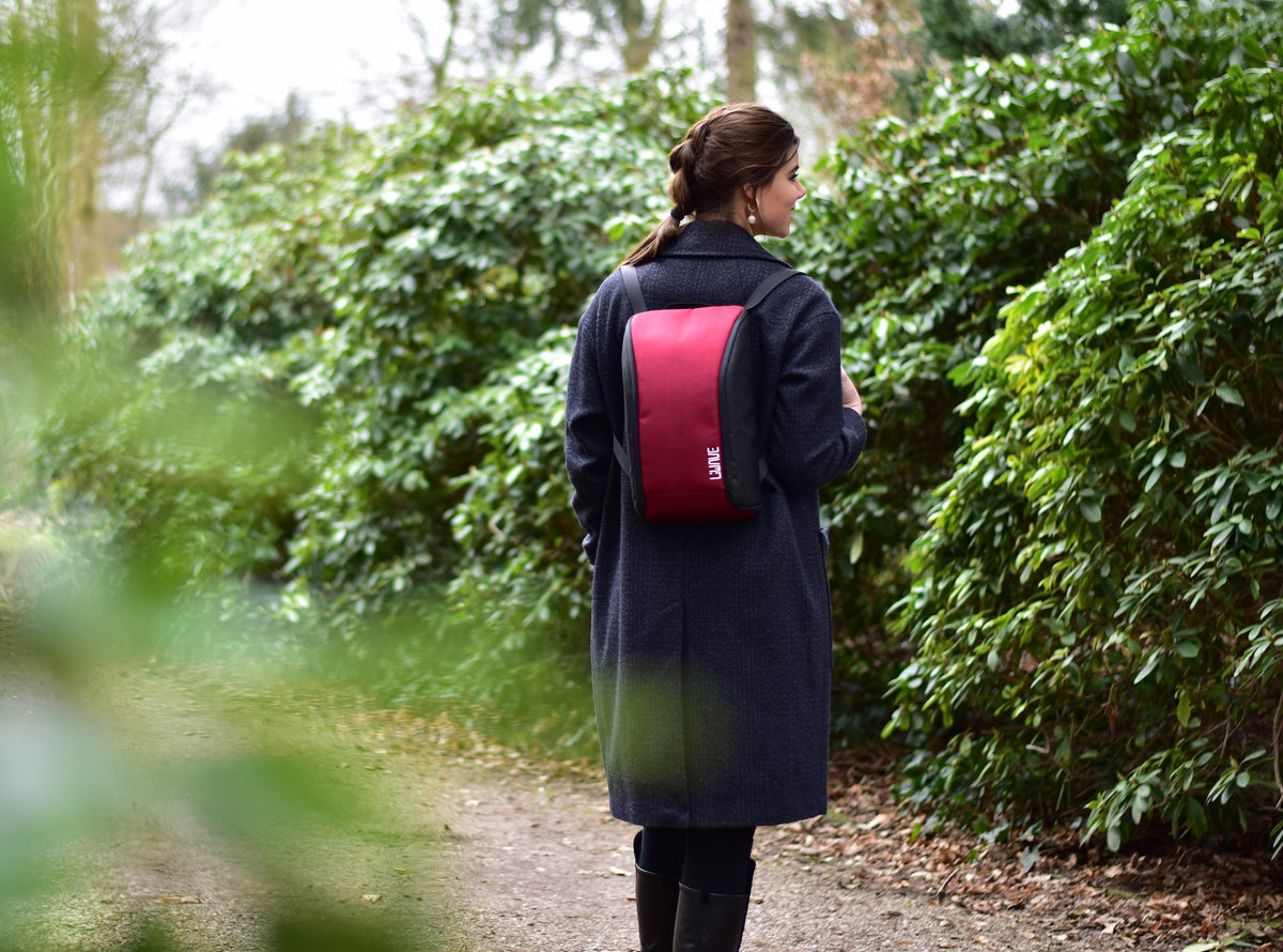 Frau mit rotem Basic LiWAVE Rucksack auf dem Rücken in der Natur